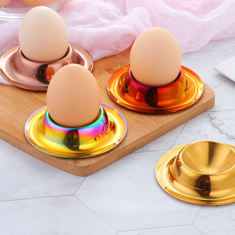 Three stainless egg holders with beige eggs in rainbow and gold finishes