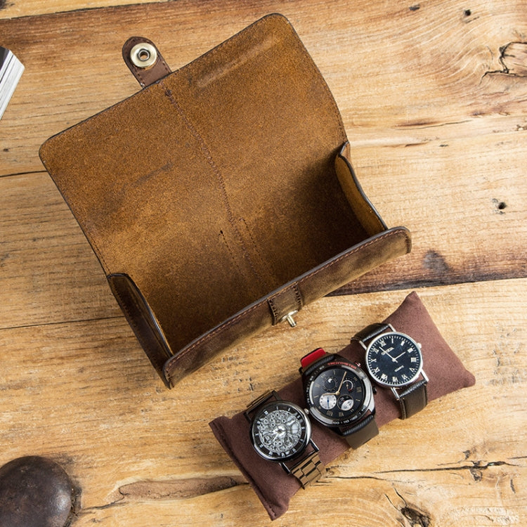 Open leather watch storage box with snap strap and watches in compartments on wood table