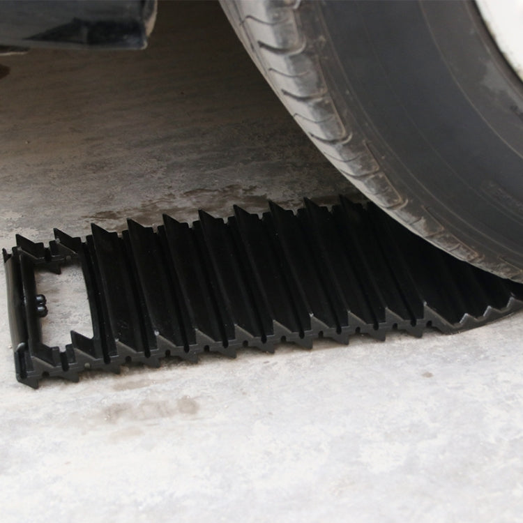 Black anti-slip traction plate positioned under a tire for grip on snow or ice