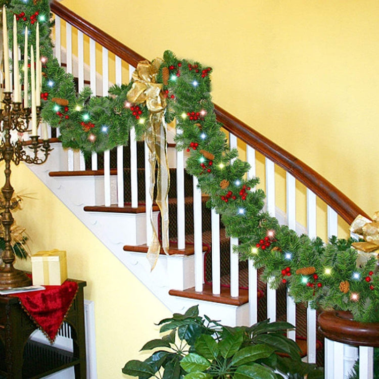 Green Christmas garland with red berries, pinecones, and warm LED lights along railing