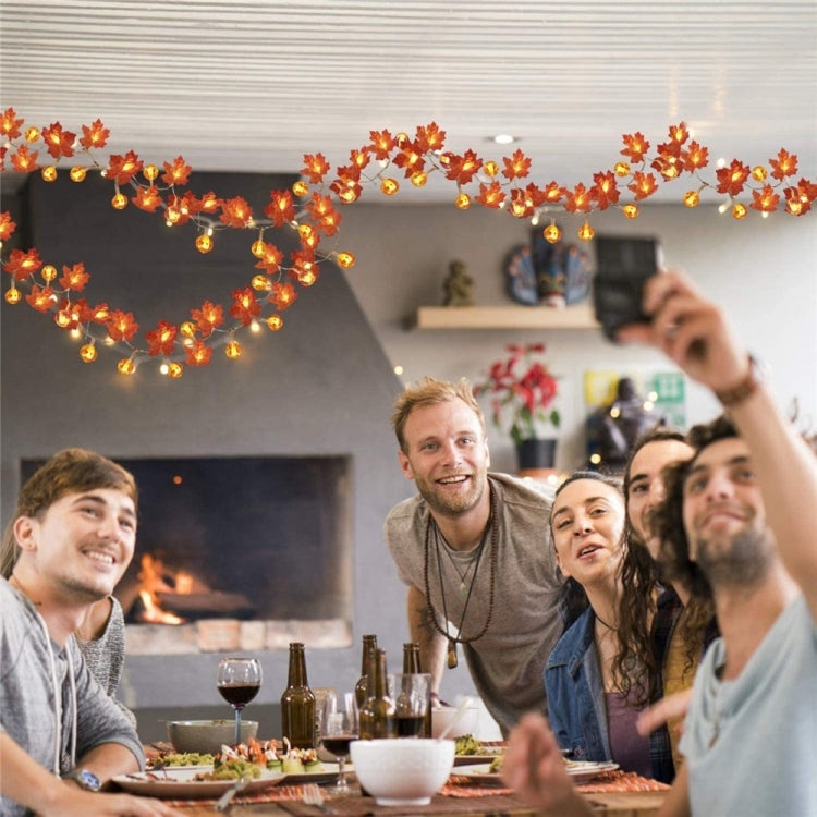 Warm amber maple leaf pumpkin lantern string lights strung above a party table
