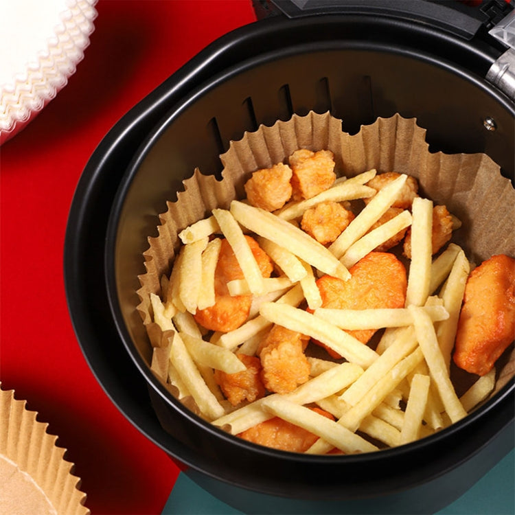 Tan baking paper liner in air fryer filled with fries and fried pieces