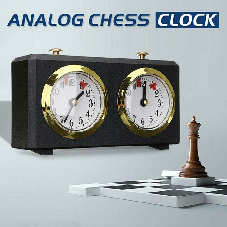 Analog chess clock with dual gold-rim dials, black case beside chess pieces