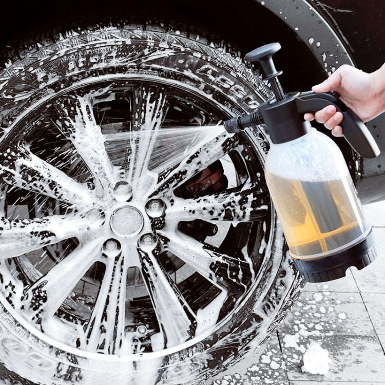 Foam sprayer applying white suds to car wheels, black nozzle and transparent bottle