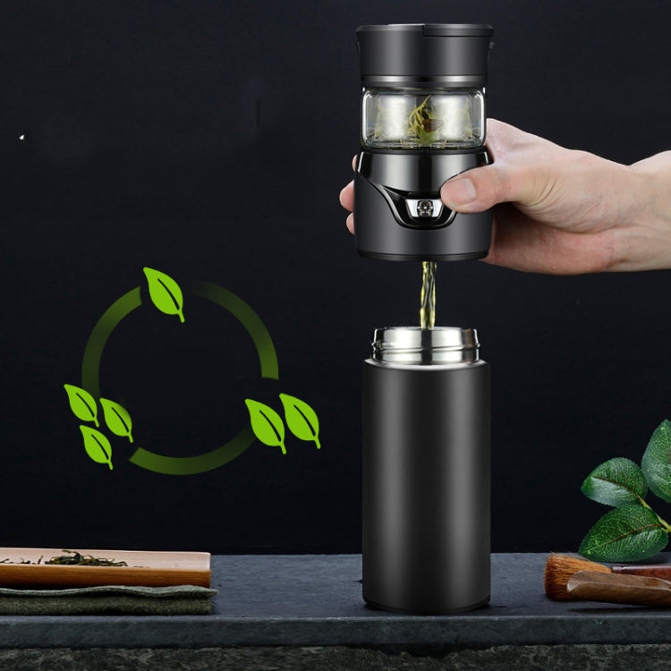 Hand holding black insulated tea separation cup, with tea pouring from glass chamber