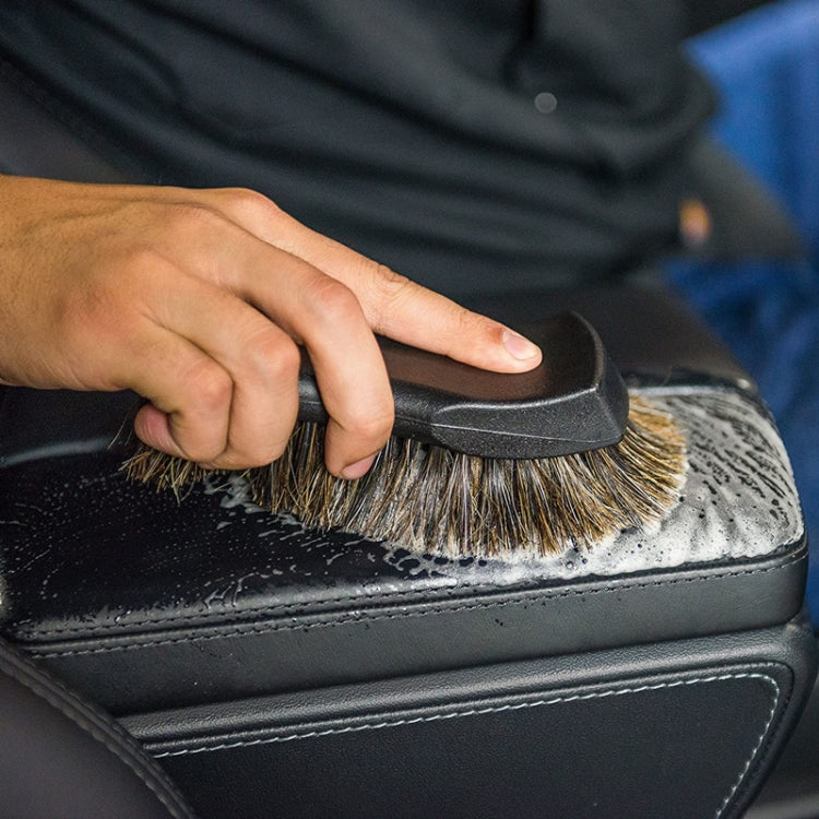 Car seat leather brush with horsehair bristles scrubbing a dark leather surface