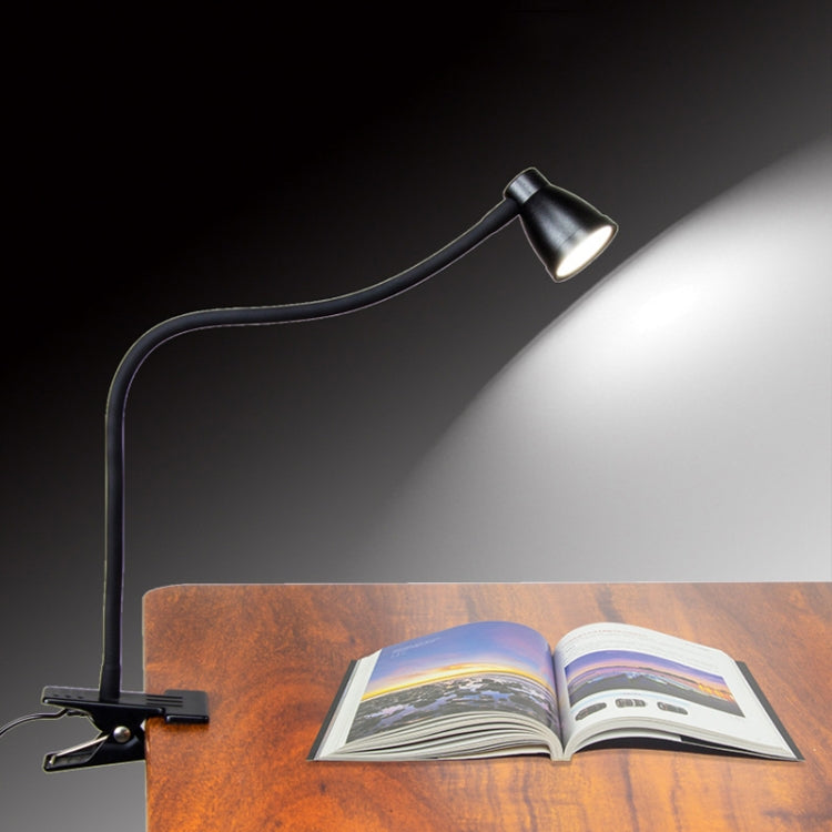 Black gooseneck desk lamp shining onto an open book from a base stand