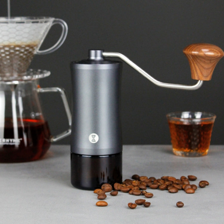 Manual coffee grinder with wooden crank handle and scattered coffee beans on table