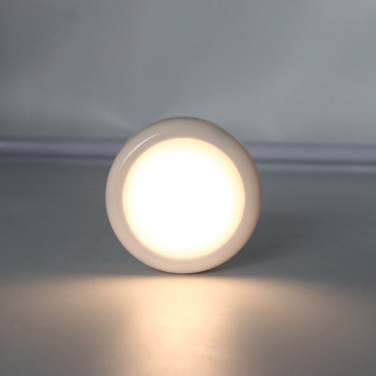 Round cabinet light puck glowing warm white from a recessed housing