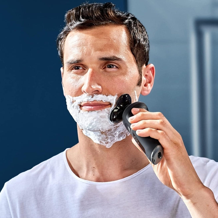 Electric razor shaver head in use, black device held against a man's cheek.