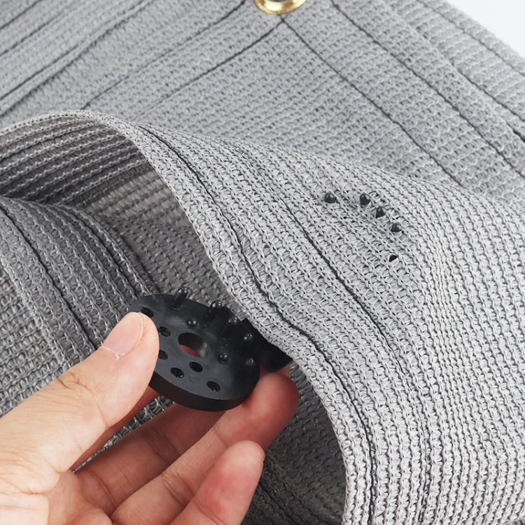 Hand holding small black net clip fastening a gray woven fabric edge