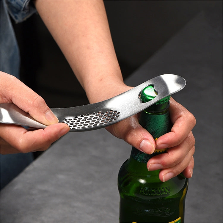 Hands holding a stainless steel boat-shaped garlic grinder near a green bottle