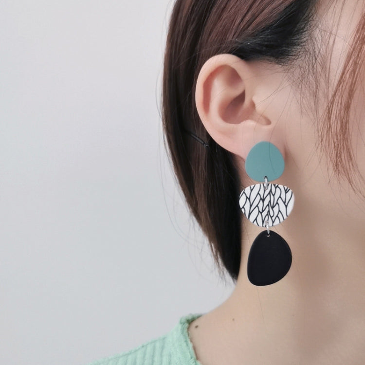 Long dangle earrings worn: teal circles with leaf-print and black oval drops