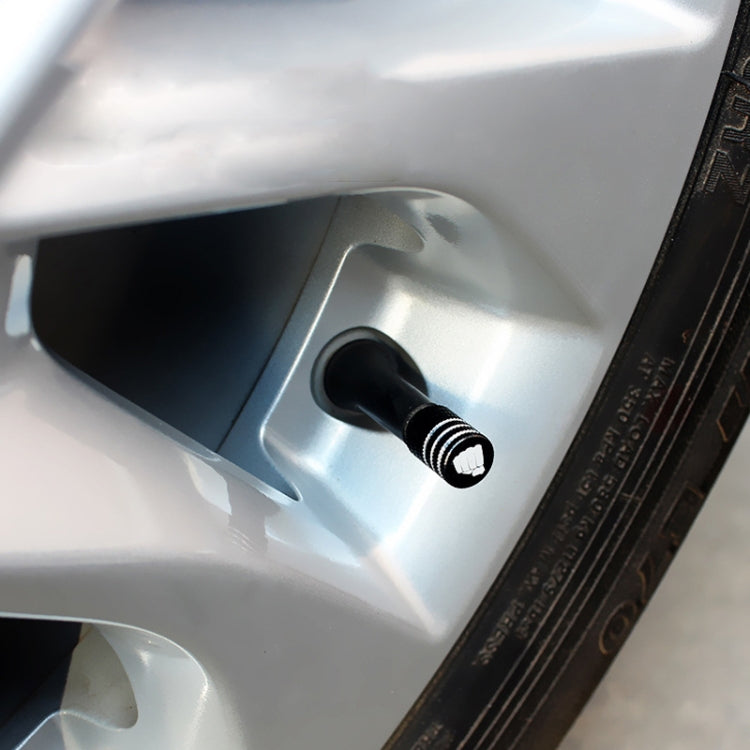 Tire valve cap installed on car wheel valve stem, black ribbed cap with white logo