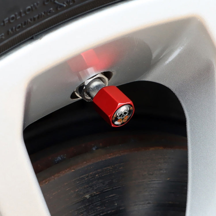 Red metal tire valve cap with skull emblem, shown installed on a car wheel valve.