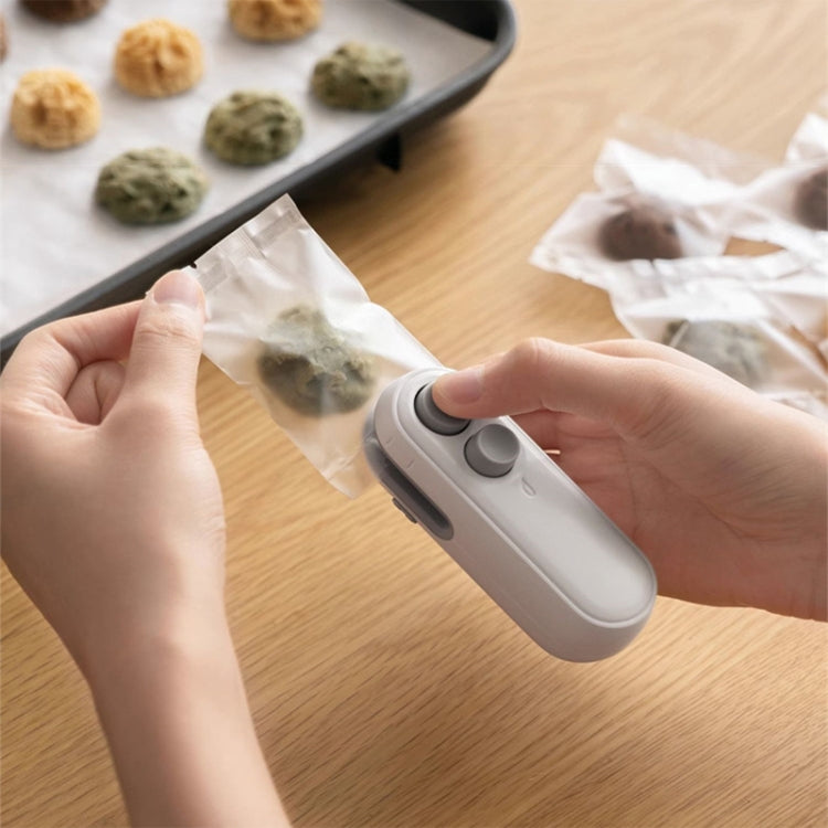 White handheld magnetic snack sealer with button, sealing a clear snack bag