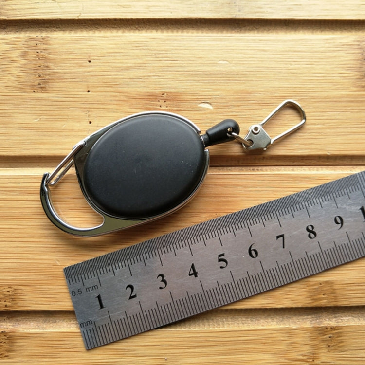 Retractable key ring holder with black oval case and retractable cord, shown with ruler on wood.