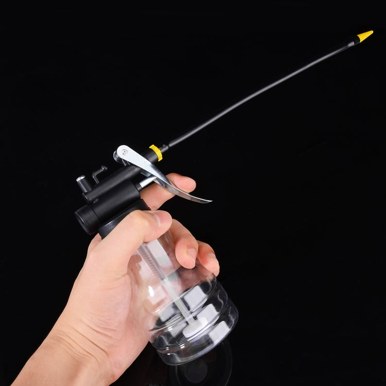Hand holding transparent plastic pump oiler with black head and yellow-tipped outlet
