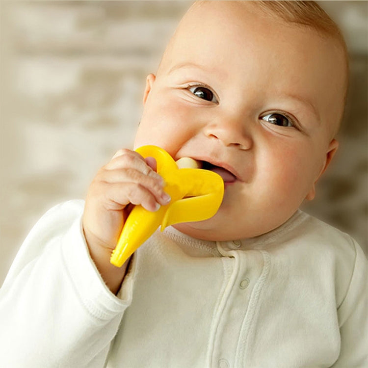 Baby holding a yellow banana-shaped silicone teether toothbrush with white bristles