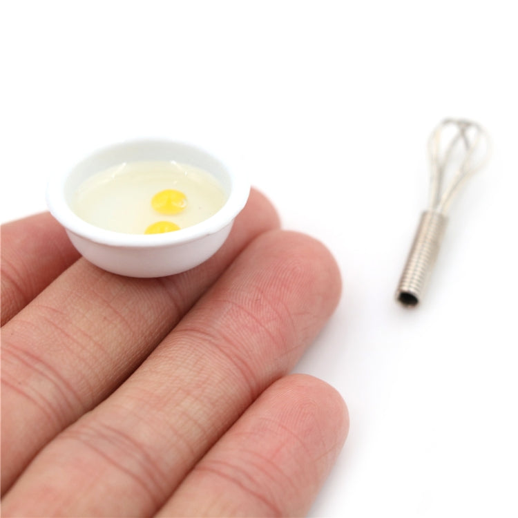 Miniature manual egg beater and small bowl with two eggs held in a hand