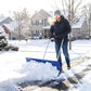 Blue wheeled snow shovel clearing snow with wide blade and adjustable long handle