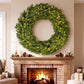 Pre-lit green evergreen wreath with warm LED lights hanging above a fireplace mantel.