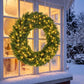 Green pre-lit Christmas wreath with warm LED lights mounted outdoors near a window.