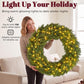 Green artificial wreath with warm LED lights held in place indoors over a sofa.