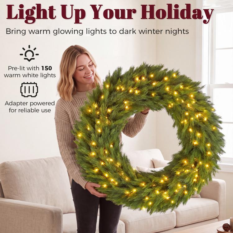 Green artificial wreath with warm LED lights held in place indoors over a sofa.