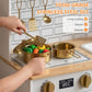 Hands using a utensil to add food pieces in a toy pot on a kids play kitchen