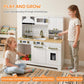 Two children playing with white kids play kitchen set; gold faucet and stove visible