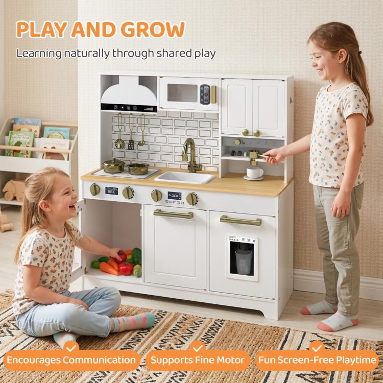 Two children playing with white kids play kitchen set; gold faucet and stove visible