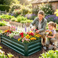 Green metal raised garden bed with slatted sides, planted with flowers beside a gardener