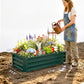 Green metal raised garden bed planter on soil, filled with flowers and herbs