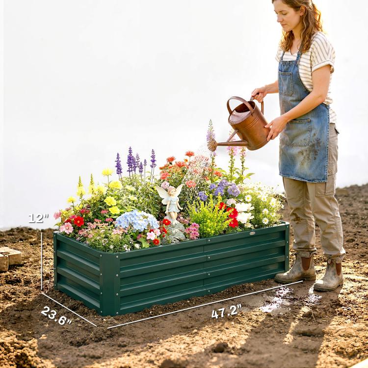 Green metal raised garden bed planter on soil, filled with flowers and herbs