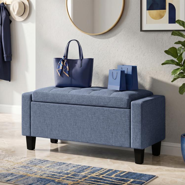 Dark blue-gray storage ottoman bench with tufted top, padded armrests, and wooden legs