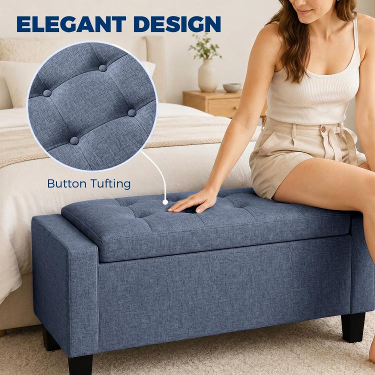 Dark blue-gray button-tufted storage ottoman bench with padded armrests and wooden legs