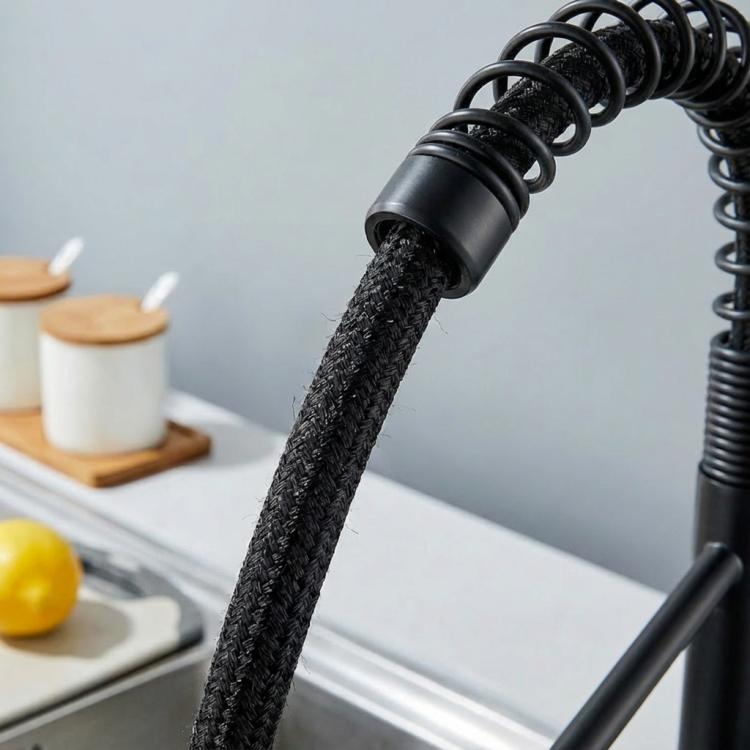 Close-up of black braided pull-down sprayer hose with water spraying from tip.