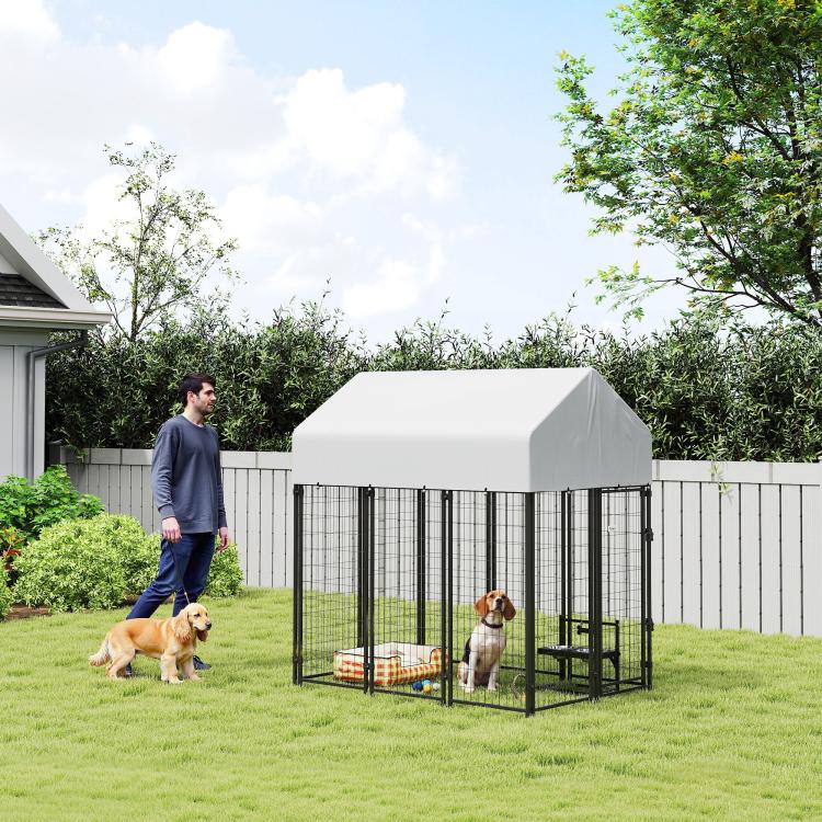 Outdoor dog kennel with peaked roof and black wire panels in yard, with sitting dogs.
