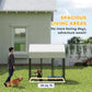 Outdoor dog kennel with peaked roof, black wire panels, dog mat inside on lawn.