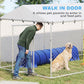 Outdoor dog kennel with walk-in access door, silver chain-link frame, sloped roof and sitting dog