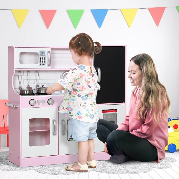 Pink kids pretend play kitchen with stovetop and sink, seen beside playing child