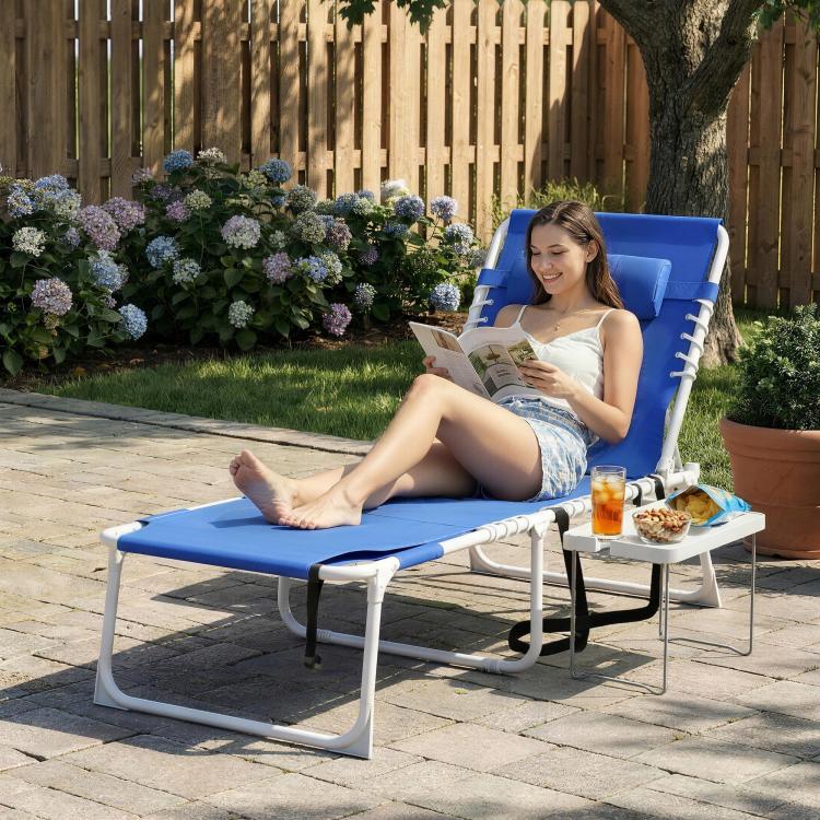 Blue folding tanning chair with face opening and side table, outdoors by a garden