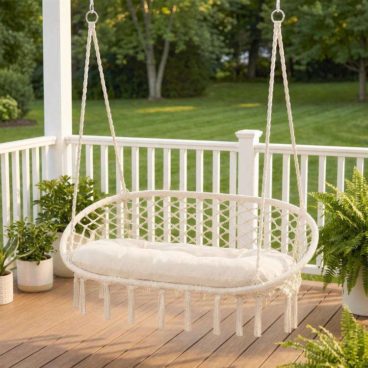 Outdoor hanging hammock chair with macrame net seat, cream cushion, and fringe ends