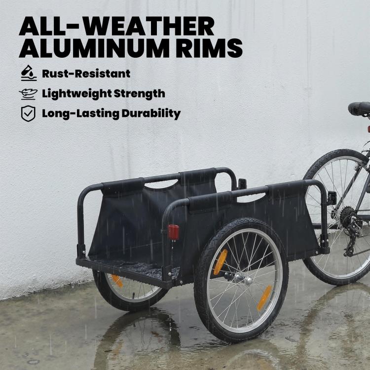 Black bike cargo trailer with open fabric bed, 16-inch pneumatic wheels, red safety flag on wet ground
