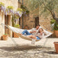 Cream two-person outdoor hammock with pillow and spreader bars between posts