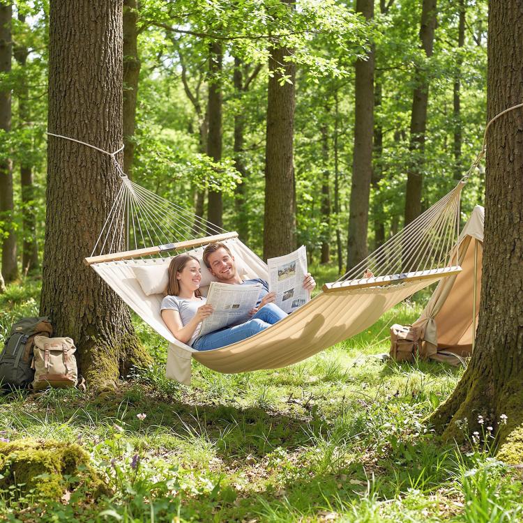 Cream hammock hanging from trees with attached pillow for two-person lounging
