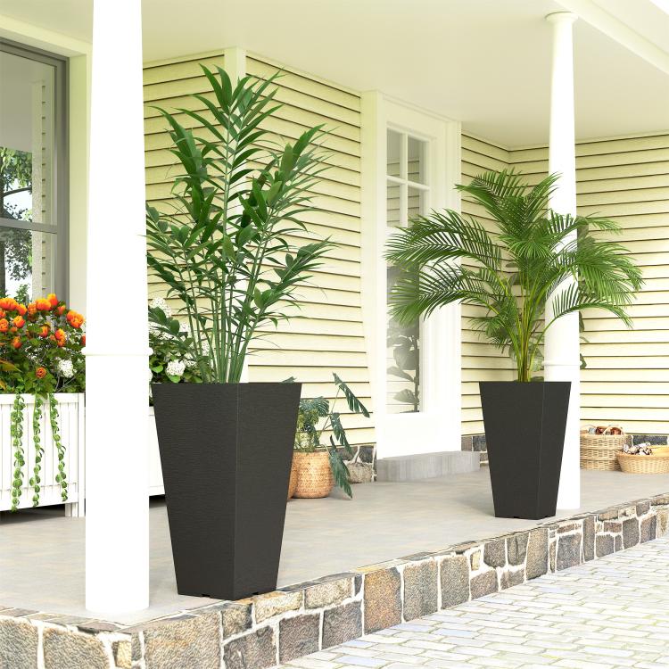 Two tall black outdoor plant pots on a stone patio with leafy plants