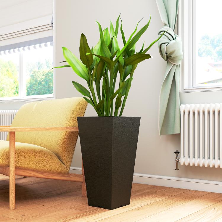 Tall black plastic planter holding green plant on indoor wooden floor