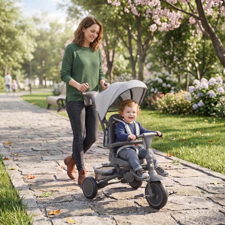 Gray kids tricycle stroller with canopy on a paved path in a park